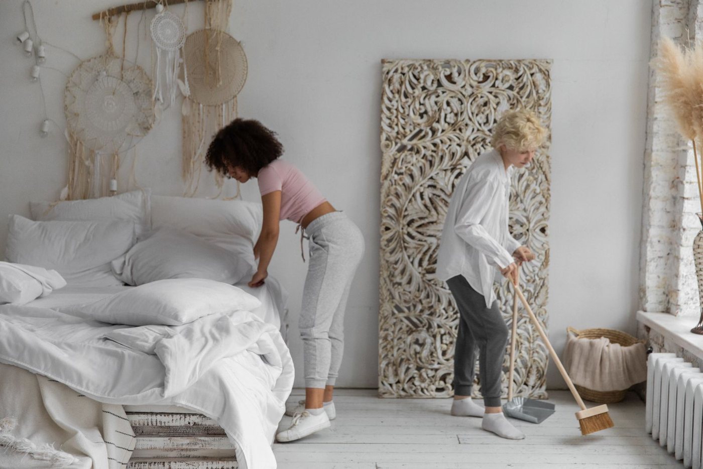 Two cleaners making a bed in a bright bedroom